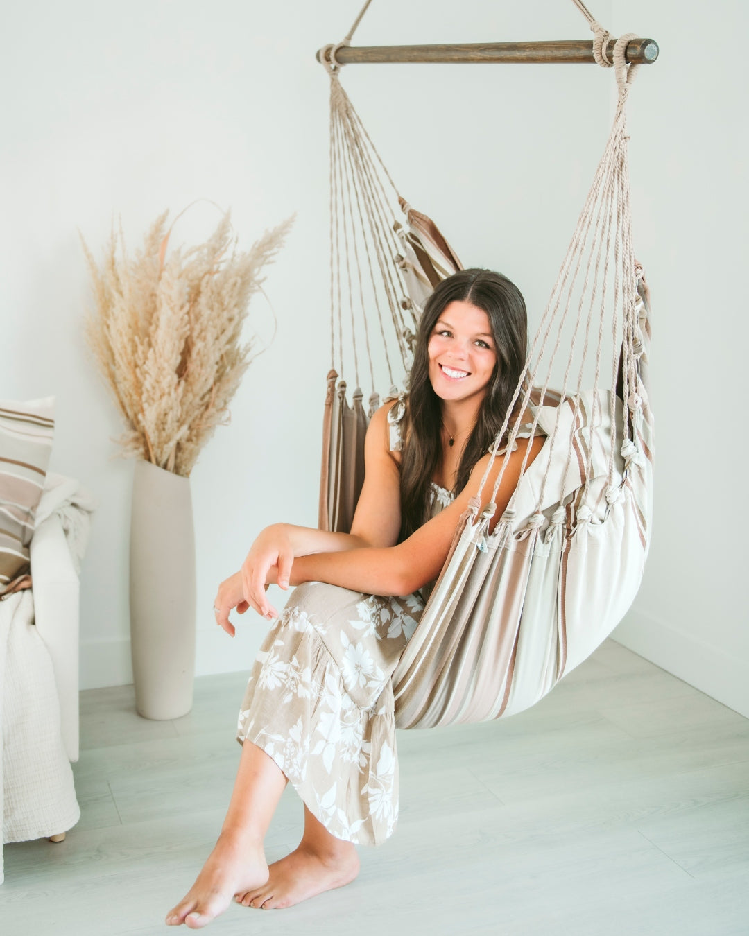 A woman sitting in a hammock chair in a bright room with boho decor elements.