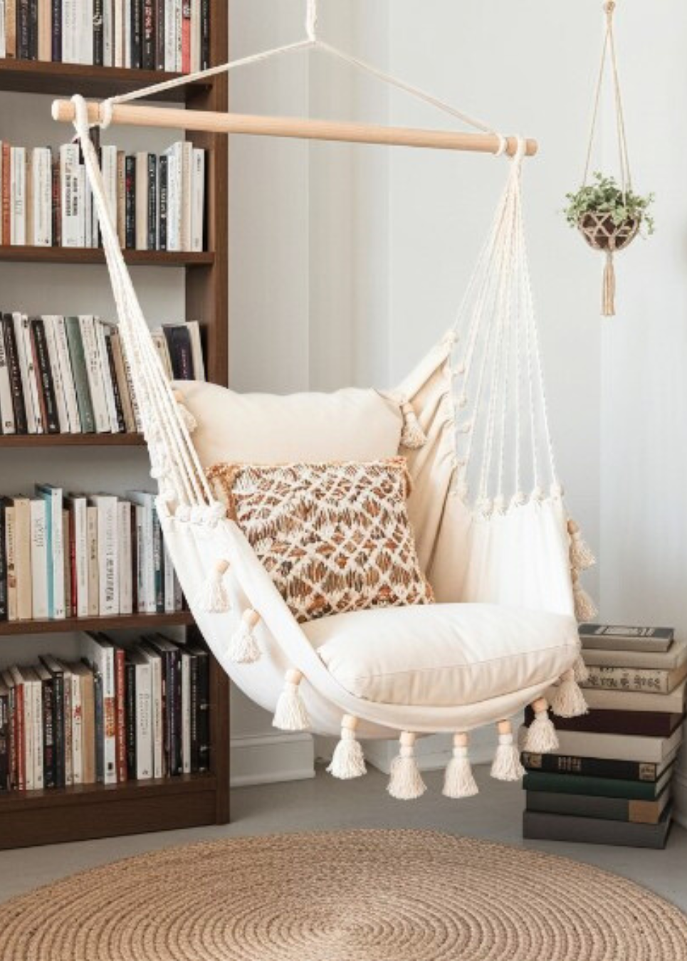 White hammock chair with tassels in a room with bookshelves and a rug.