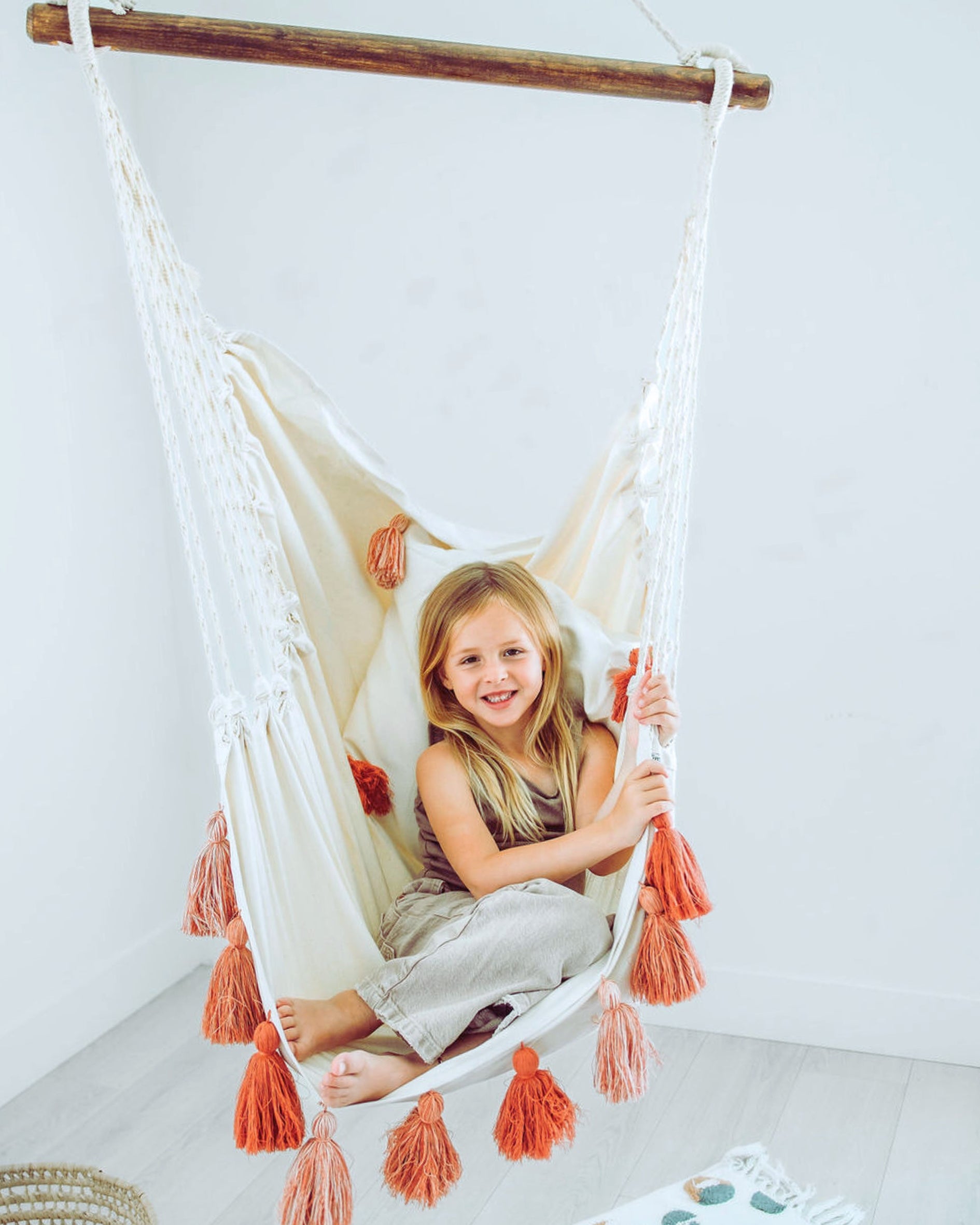 girl sitting in a small hammock chair with pink tassels