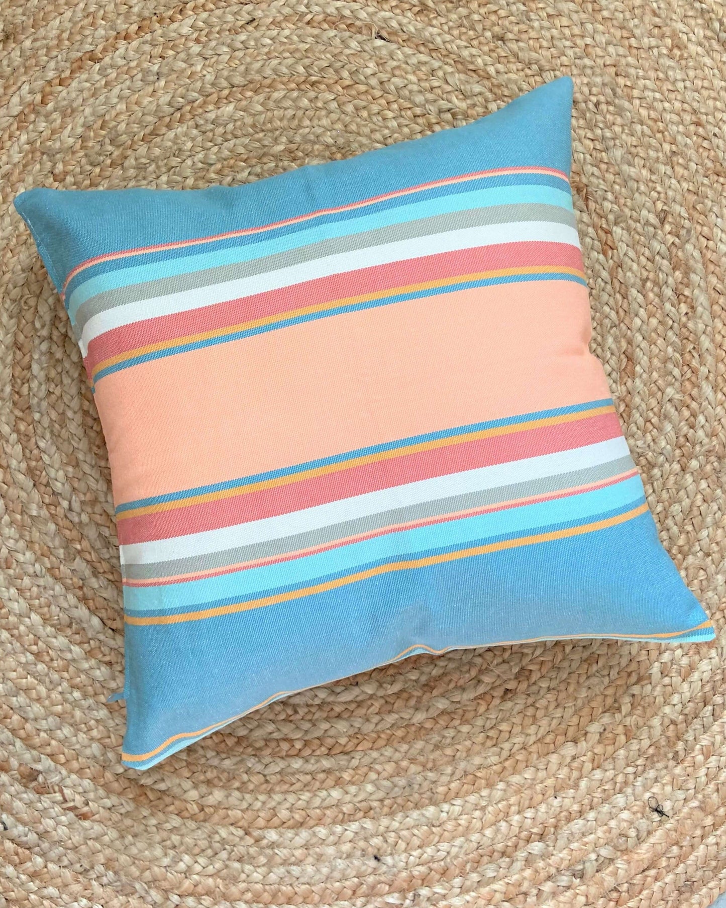 pastel striped pink and light blue pillow lying on a jute rug