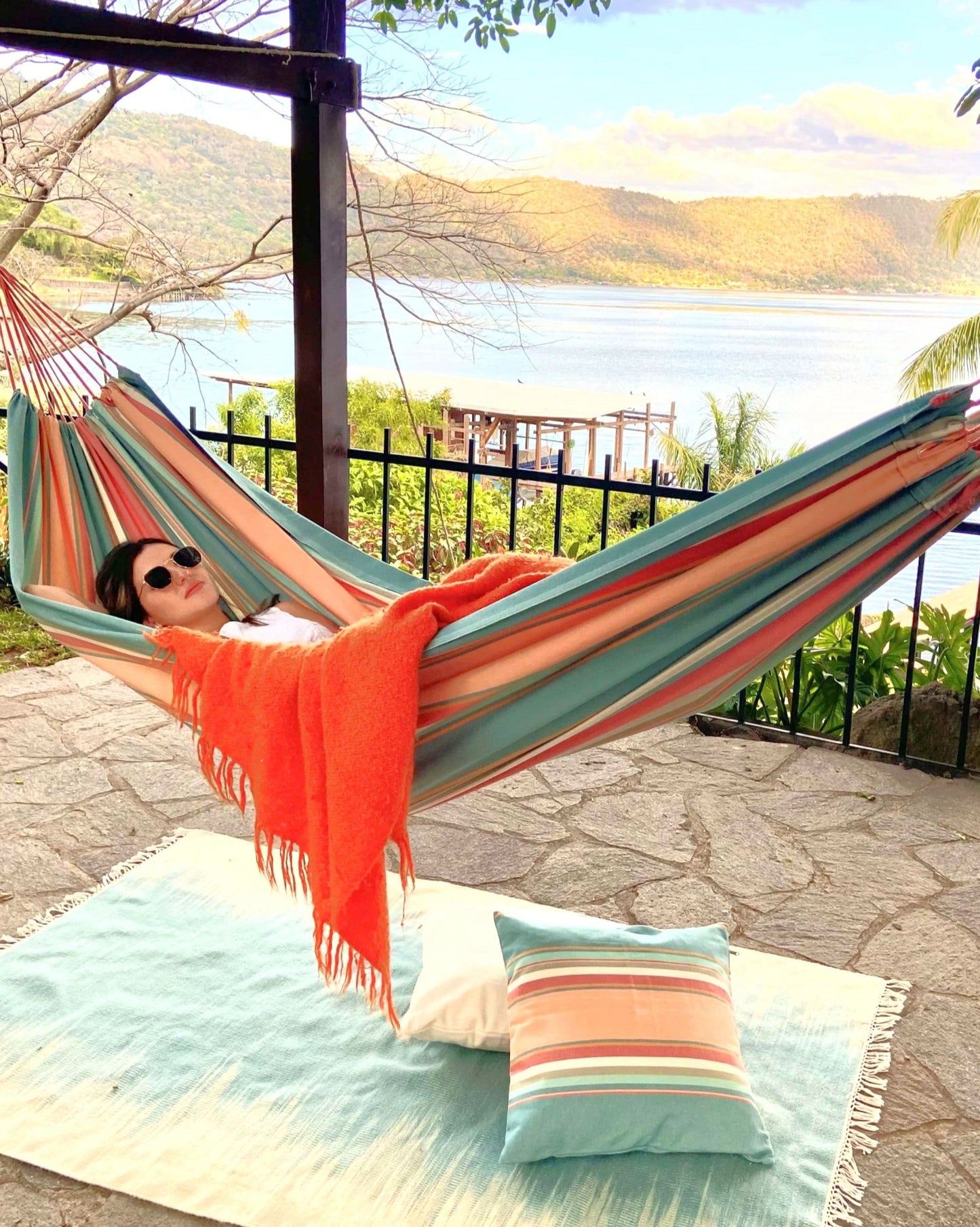 woman sleeping on a striped pink and light blue hammock. She is covered with an orange throw blanket.