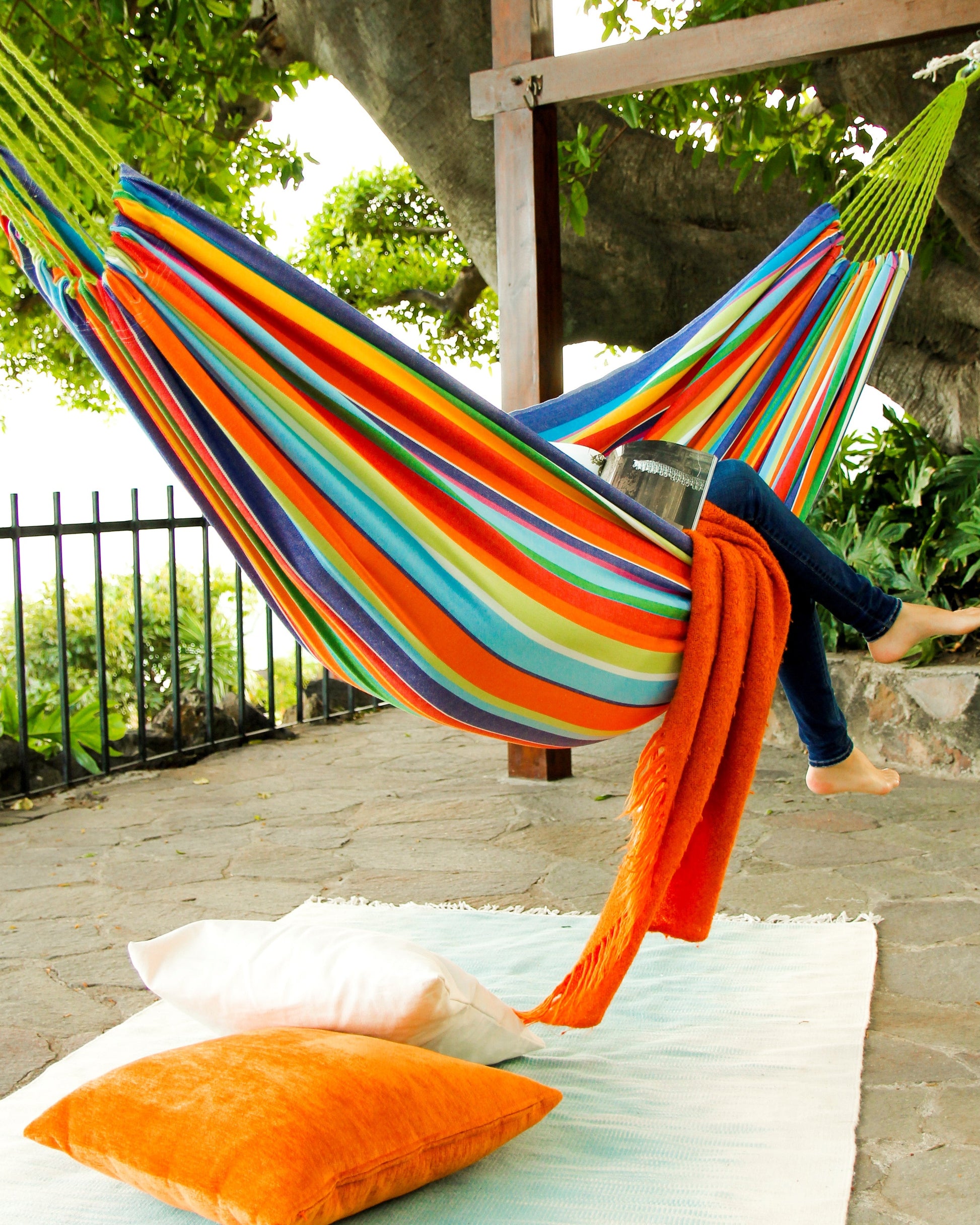 Colorful striped hammock with a person sitting in it, surrounded by greenery outdoors