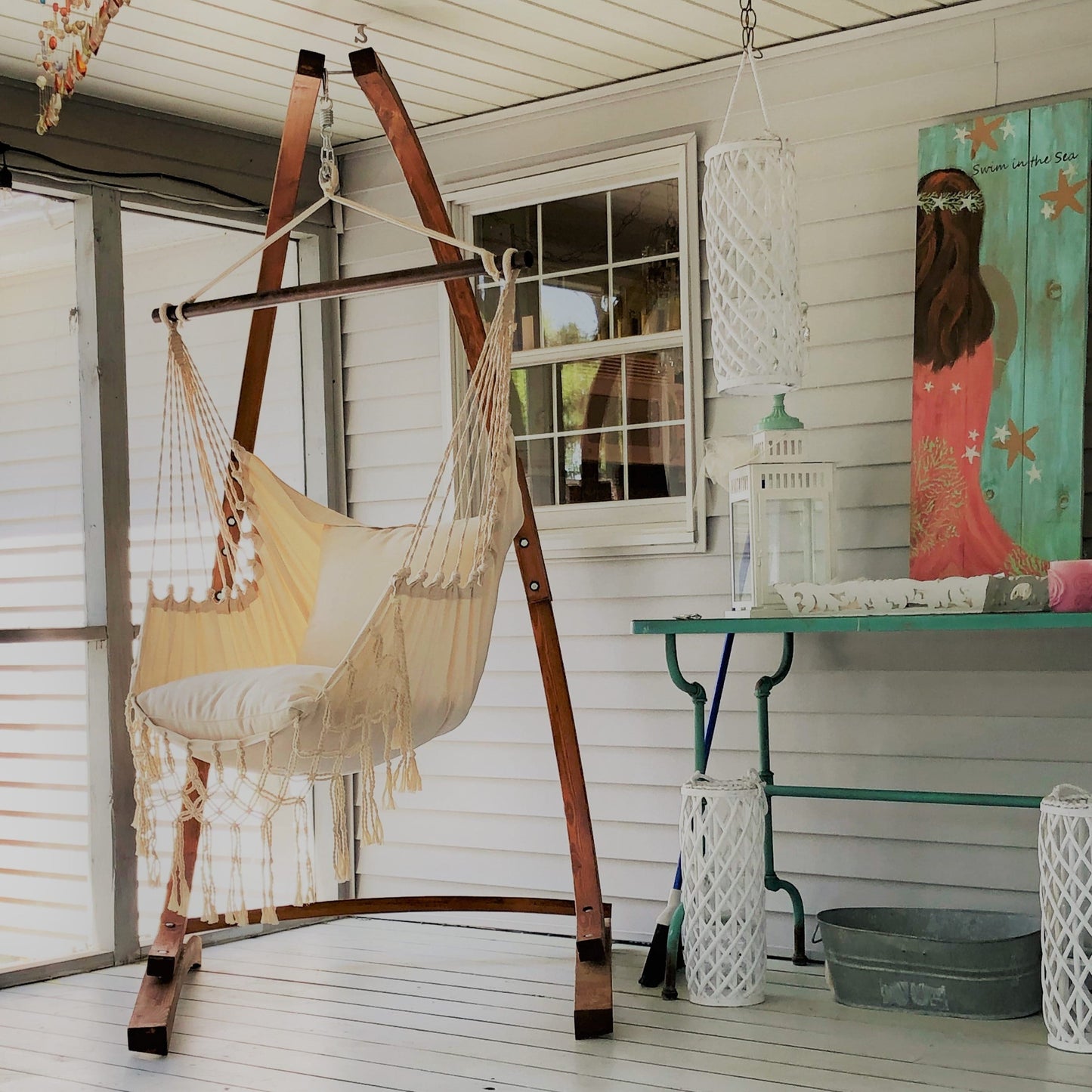 White Macrame hammock swing chair on a wooden chair stand  in a covered patio'