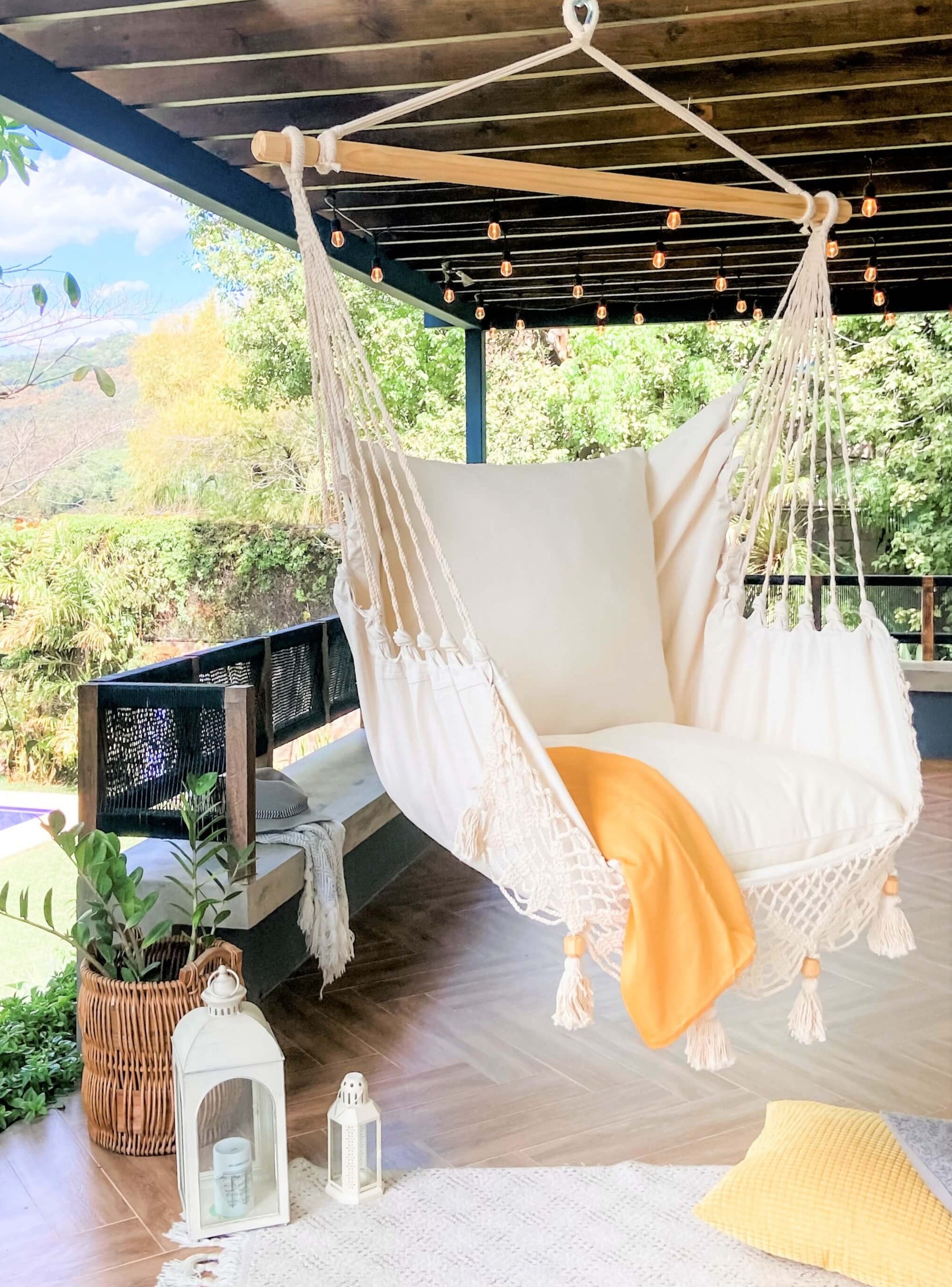 patio with hanging lights and a macrame hammock swing chair with a yellow throw on top
